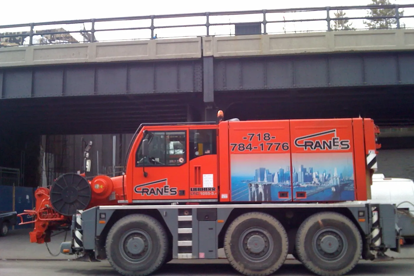 Compact city crane with outriggers set up beside an overpass
