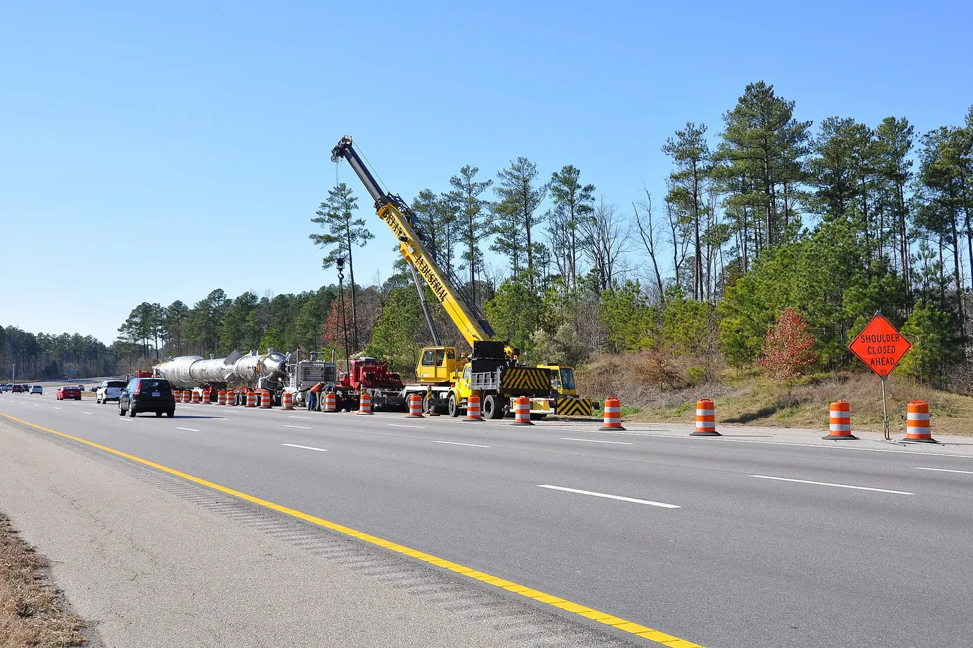 Truck crane lifting a heavy vessel beside a highway